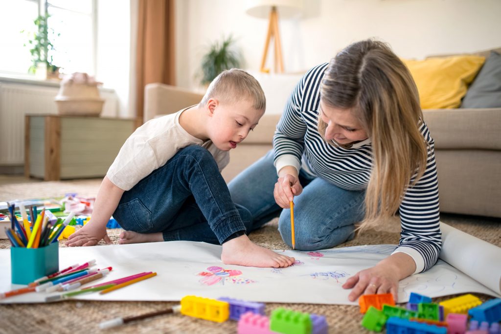 Mother and boy with down syndrome sitting on the floor drawing together-min